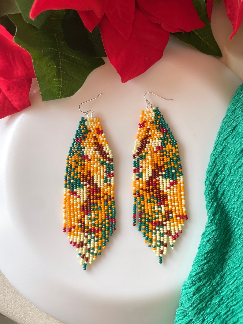 May include: A pair of long, beaded earrings with a colourful, geometric pattern in shades of yellow, orange, green, red, and white. The earrings are made of small, round beads and have a teardrop shape.