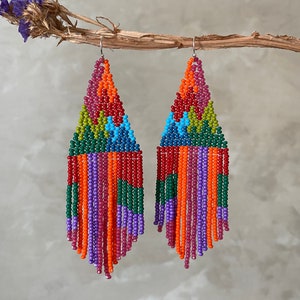 May include: A pair of colourful beaded earrings with a geometric design and fringe. The earrings are made with red, orange, yellow, green, blue, and purple beads.