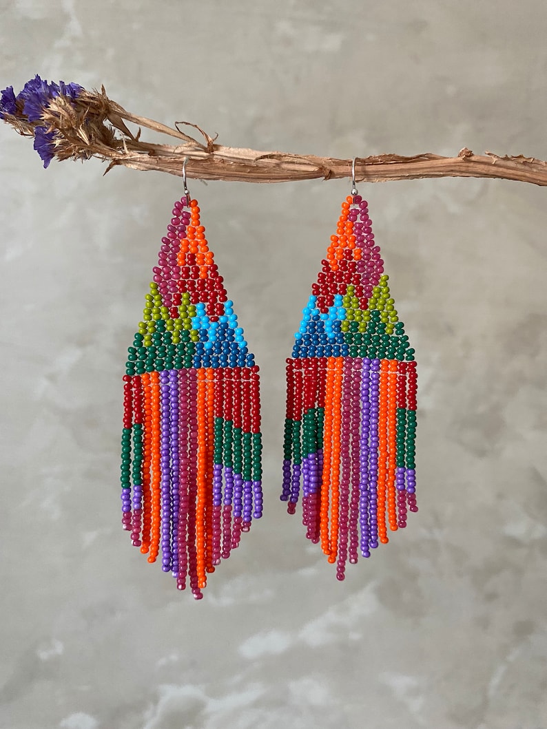 May include: A pair of colourful beaded earrings with a geometric design and fringe. The earrings are made with red, orange, yellow, green, blue, and purple beads.