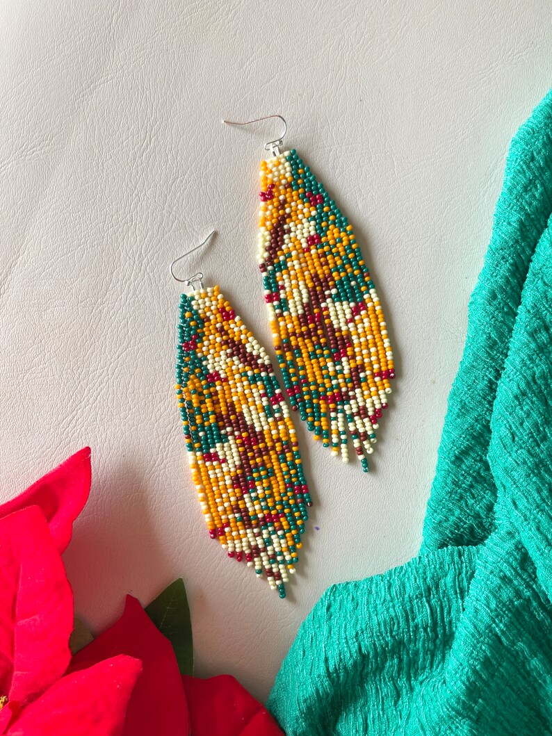 May include: A pair of long, beaded earrings with a geometric pattern in shades of yellow, green, white, and red. The earrings are made with small, seed beads and have a fringe-like design.
