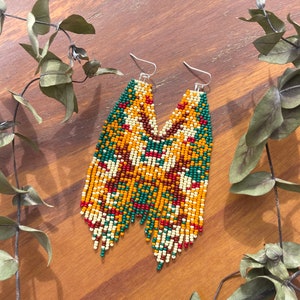 May include: A pair of long, beaded earrings with a geometric pattern in shades of green, red, yellow, and white.