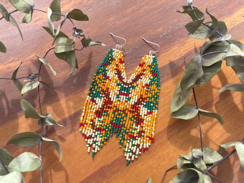 May include: A pair of long, beaded earrings with a geometric pattern in shades of green, red, yellow, and white.