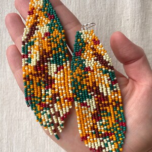May include: A pair of long, beaded earrings with a geometric pattern in shades of red, orange, yellow, green, and white.