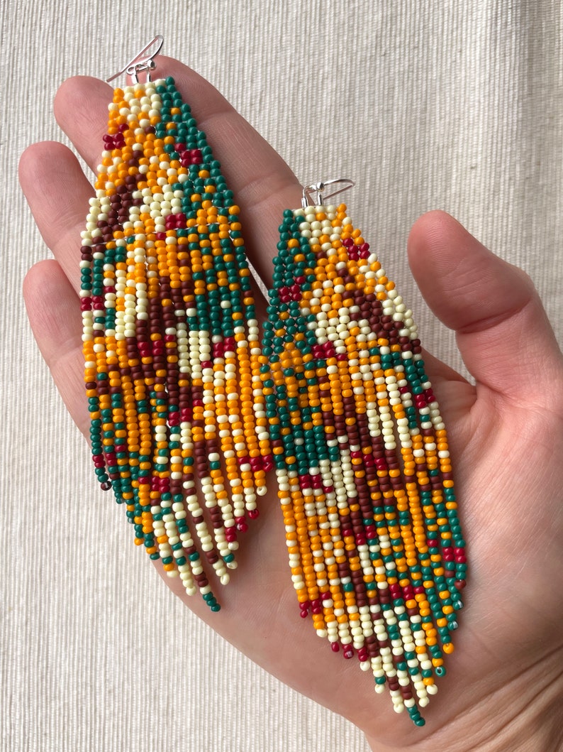 May include: A pair of long, beaded earrings with a geometric pattern in shades of red, orange, yellow, green, and white.