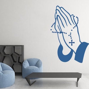 May include: Blue wall decal of two hands clasped in prayer with a rosary around the wrists. The rosary has a cross at the end.