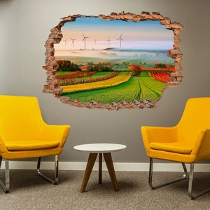 Puede incluir: Un adhesivo de pared 3D que presenta un paisaje escénico con aerogeneradores, colinas onduladas y un cielo brumoso de la mañana. La calcomanía se coloca en una pared gris con dos sillas amarillas y una mesa pequeña en frente.