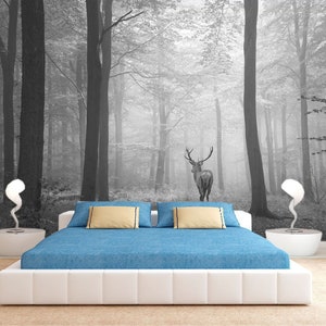 May include: A white bed with a blue comforter and two beige pillows sits in front of a black and white photo mural of a deer standing in a foggy forest.