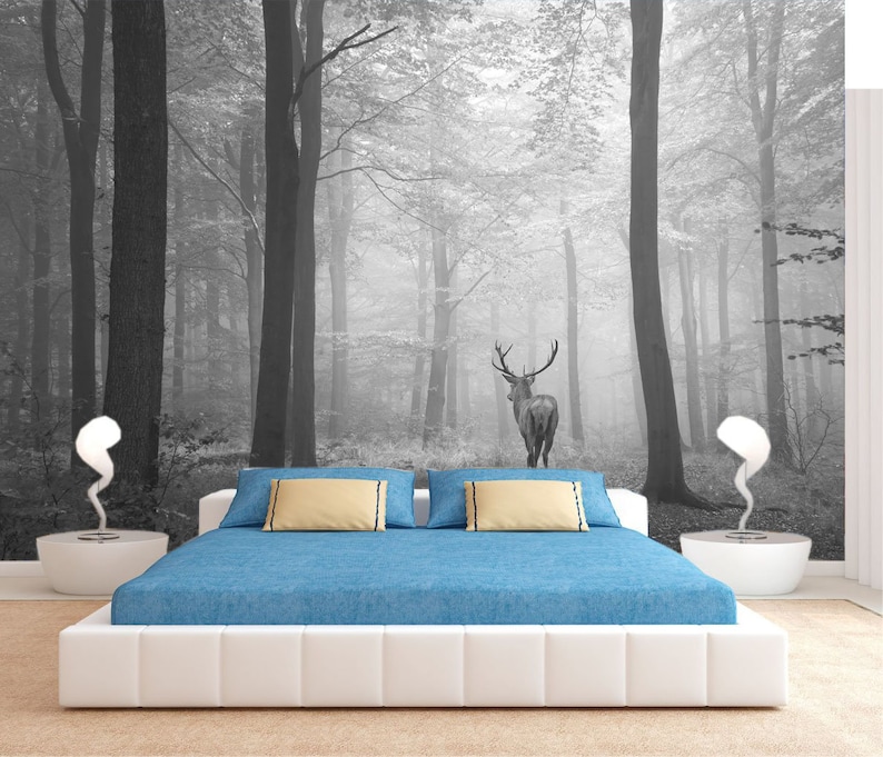 May include: A white bed with a blue comforter and two beige pillows sits in front of a black and white photo mural of a deer standing in a foggy forest.