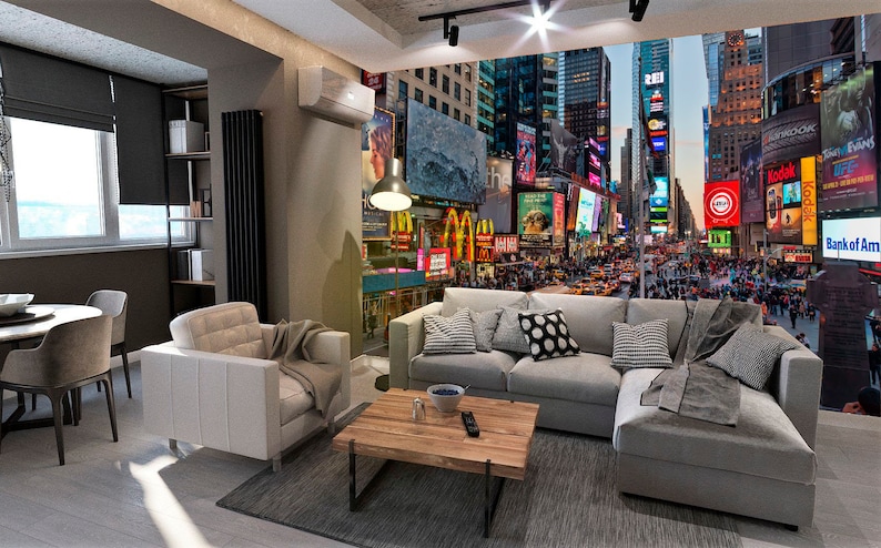 May include: A living room with a gray sectional sofa and a white armchair. The wall behind the sofa features a mural of Times Square in New York City at night. The mural is filled with bright lights and advertisements.