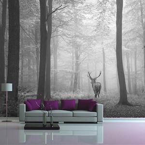 May include: A black and white photo of a deer standing in a foggy forest. The deer is facing away from the camera and has large antlers. The forest is dense with trees and the ground is covered in leaves.