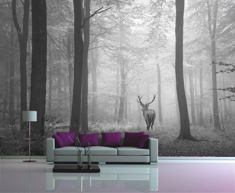 May include: A black and white photo of a deer standing in a foggy forest. The deer is facing away from the camera and has large antlers. The forest is dense with trees and the ground is covered in leaves.