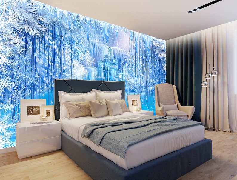 Op de afbeelding: Een slaapkamer met een blauwe en witte muurschildering die een bevroren bos en kasteel voorstelt. Het bed heeft een blauw hoofdeinde en een wit en blauwe deken. Er is een wit nachtkastje met een lamp en een fotolijst erop. Een beige fauteuil staat in de hoek van de kamer.