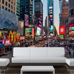 May include: A colorful cityscape mural featuring Times Square in New York City with bright lights, billboards, and a crowd of people walking on the street. The mural is displayed on a wall behind a white couch and a coffee table.