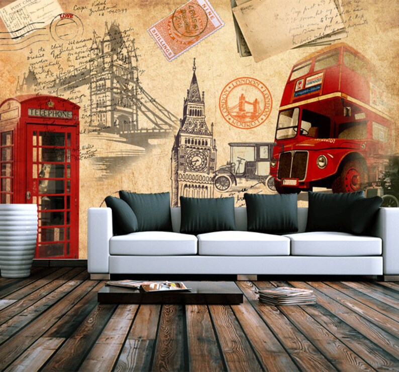 May include: A vintage-style illustration of London landmarks, including Big Ben, a red double-decker bus, a red telephone booth, and Tower Bridge. The illustration is printed on a wall behind a white couch with black pillows.