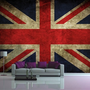 Pode incluir: Um mural de papel de parede com a bandeira da União Jack desbotada em cores vermelho, branco e azul. A bandeira é exibida em uma parede em uma sala de estar com um sofá cinza e um abajur.