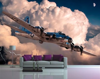 May include: A silver B-17 bomber plane flies through a cloudy sky. The plane has the words "GJ Virgin II" on the side. The plane is flying towards a large, fluffy cloud.