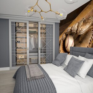 May include: A bedroom decorated in shades of grey and white. The bedroom features a bed with a grey headboard, white bedding, and a grey knitted throw blanket. The wall behind the bed has a mural of a baseball glove catching a baseball. The bedroom also has a wardrobe with glass doors, a bedside table, and a television.