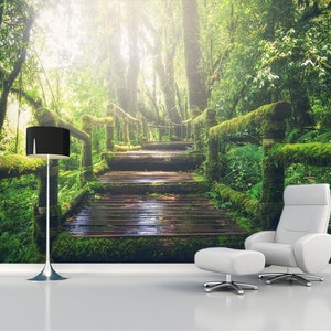 May include: A wooden walkway leads through a lush green forest with moss covered trees and a black floor lamp.