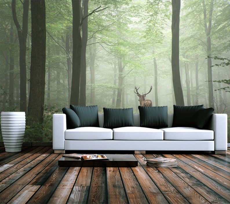 May include: A white couch with black pillows sits in front of a wall mural depicting a foggy forest with a deer standing in the middle.