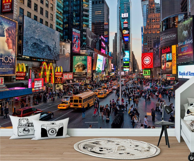 May include: A busy street scene in New York City with tall buildings, bright lights, and many people walking around. There are many billboards and signs with advertisements for various businesses, including McDonald's, Kodak, and Bank of America.