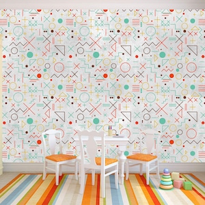 Op de afbeelding: Een witte muur met een geometrisch patroon in rood, oranje, geel, blauw en bruin. Het patroon bevat cirkels, vierkanten, driehoeken en lijnen. Er staan drie witte stoelen met oranje kussens voor de muur.