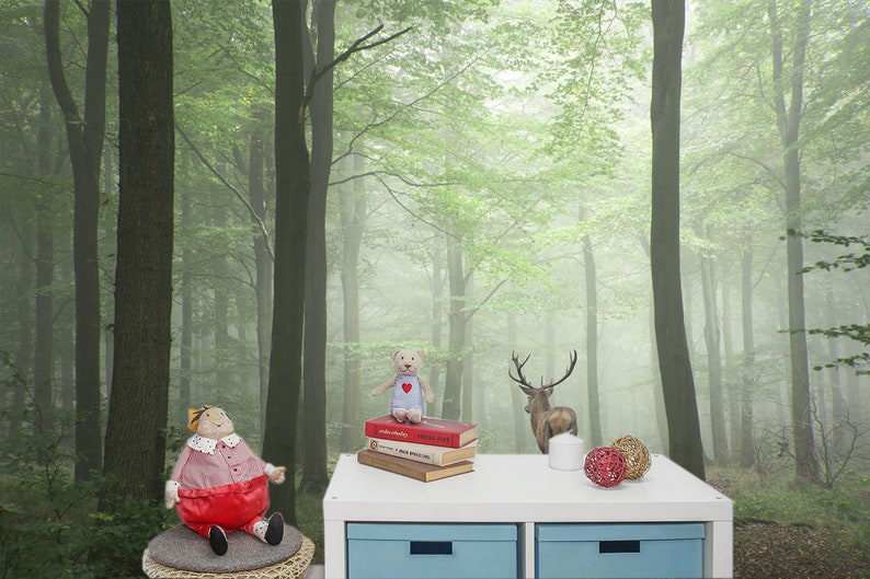 May include: A white table with two drawers sits in front of a foggy forest scene wallpaper. On the table are a stack of books, a teddy bear, a deer figurine, and two decorative balls.
