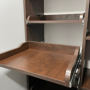May include: A brown wooden pull-out shelf with a smooth surface and silver metal rails. The shelf is mounted to a brown wooden cabinet.