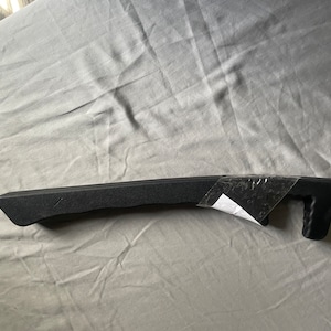 May include: Black plastic chain guide for a bicycle. The guide has a textured surface and a small handle on the end.