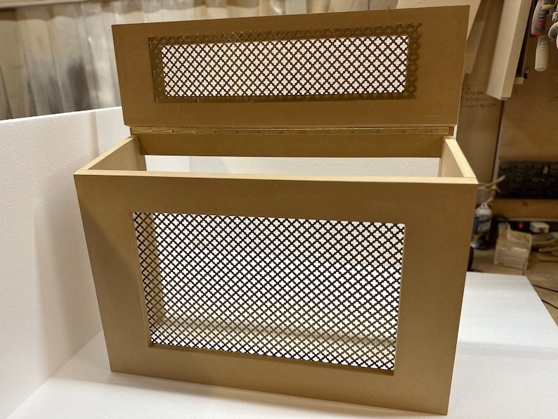 May include: A wooden box with a hinged lid and a decorative metal mesh panel on the front and lid. The box is light brown in color and has a simple design.