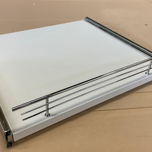 May include: White pull-out shelf with a chrome railing. The shelf is designed for kitchen cabinets.