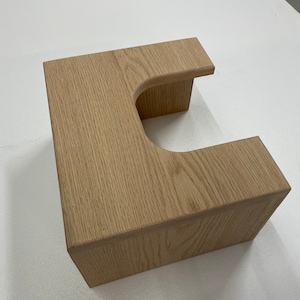 May include: A light wood step stool with a U-shaped cutout in the top. The stool is made of solid wood and has a natural finish.