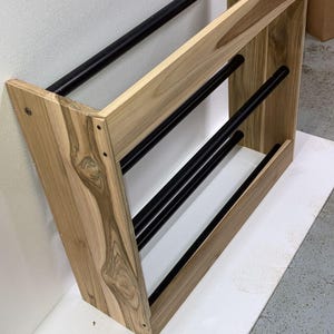 May include: A wooden shoe rack with three black metal shelves. The rack is made of light brown wood with dark brown streaks.