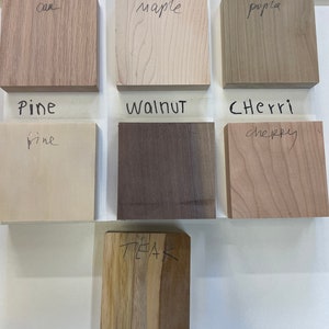 May include: A close-up of nine wood samples labeled with their names: Oak, Maple, Poplar, Pine, Walnut, Cherry, and Teak. The wood samples are arranged in a grid pattern on a white surface.