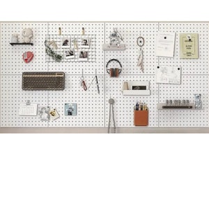 Op de afbeelding: Een wit prikbord met verschillende items eraan bevestigd, waaronder een toetsenbord, een kalender, een draadgaas met foto's, een klein knuffeldier, een koptelefoon, een klein plankje met een bruine leren potloodhouder en een klein plankje met een rij kleine glazen flesjes.
