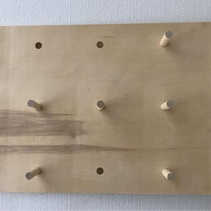 May include: A light wood pegboard with 10 wooden pegs and 5 holes. The pegboard is a great way to organize and display items.