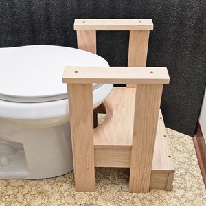 May include: A wooden toilet training step stool with two steps. The stool is made of natural wood and has a simple design.