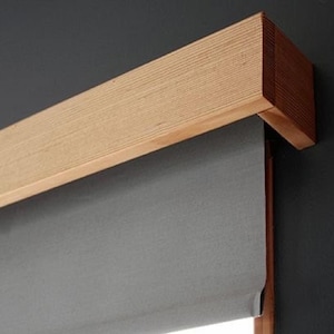 May include: A gray fabric roller shade with a wooden valance. The valance is a light brown color and has a wood grain texture.