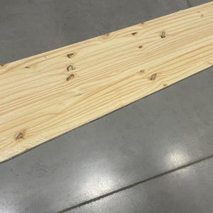May include: A plain, light brown wooden board with a smooth surface. The board is made of pine wood and has a natural grain pattern.