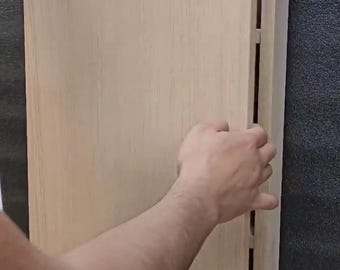 May include: A rectangular light-colored wooden cabinet door with a smooth, flat surface. The door is attached to a matching wooden frame structure with visible internal shelving supports along the side edge of the unit.
