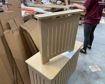 May include: A light brown wooden radiator cover with vertical slats. The cover is sitting on top of a similar cover with a flat top.