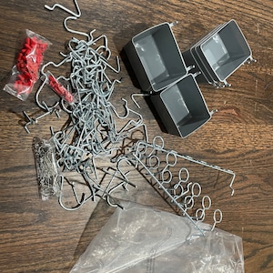 Op de afbeelding: Een set grijze plastic opbergbakken met metalen haken en een zak met verschillende metalen haken. Er zijn ook twee zakken met rode plastic doppen.