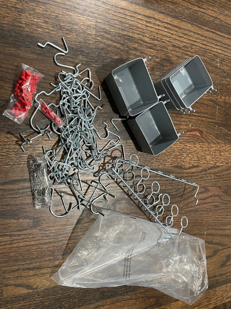 Op de afbeelding: Een set grijze plastic opbergbakken met metalen haken en een zak met verschillende metalen haken. Er zijn ook twee zakken met rode plastic doppen.