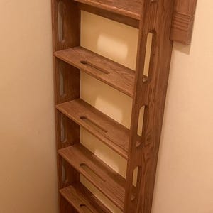 May include: A tall, wooden, corner shelf unit with multiple shelves. The unit is made of a light brown wood and has a series of cut-out designs along the sides. The shelves have a curved design.