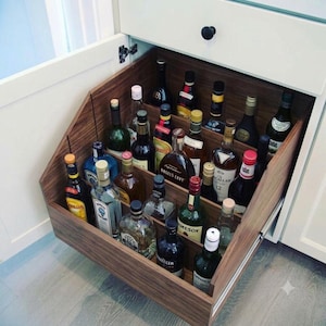 May include: A pull-out wooden drawer organizer containing various glass liquor bottles of different shapes and sizes. The organizer features tiered shelving with dividers to keep the bottles upright and organized within the kitchen cabinet.