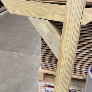 May include: Close-up of unfinished wooden beams and planks, likely for construction or carpentry projects. The wood has a natural, light-yellow color with visible grain patterns. The beams are joined at an angle, suggesting a structural element.