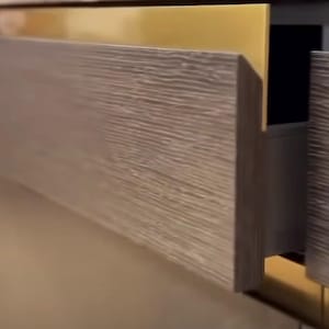 May include: A close-up of a wooden drawer with a gold metal handle. The drawer is open and the inside is visible.