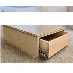 May include: A light wood storage box with a drawer that is partially open. The drawer has a silver metal slide.