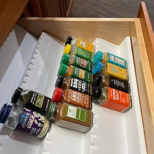 May include: A white drawer organizer with a variety of spice jars, including garlic, bay leaves, citrusy garlic, seasoning salt, and BBQ 101. The jars are arranged in rows and are mostly glass with colorful labels.