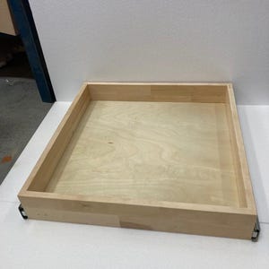 May include: A wooden drawer box with a light wood finish. The drawer box is empty and has a simple design.