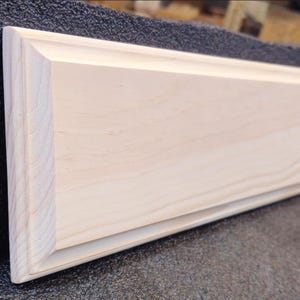 May include: A plain, unfinished wooden plaque with a raised edge. The plaque is made of light-colored wood and has a smooth surface.